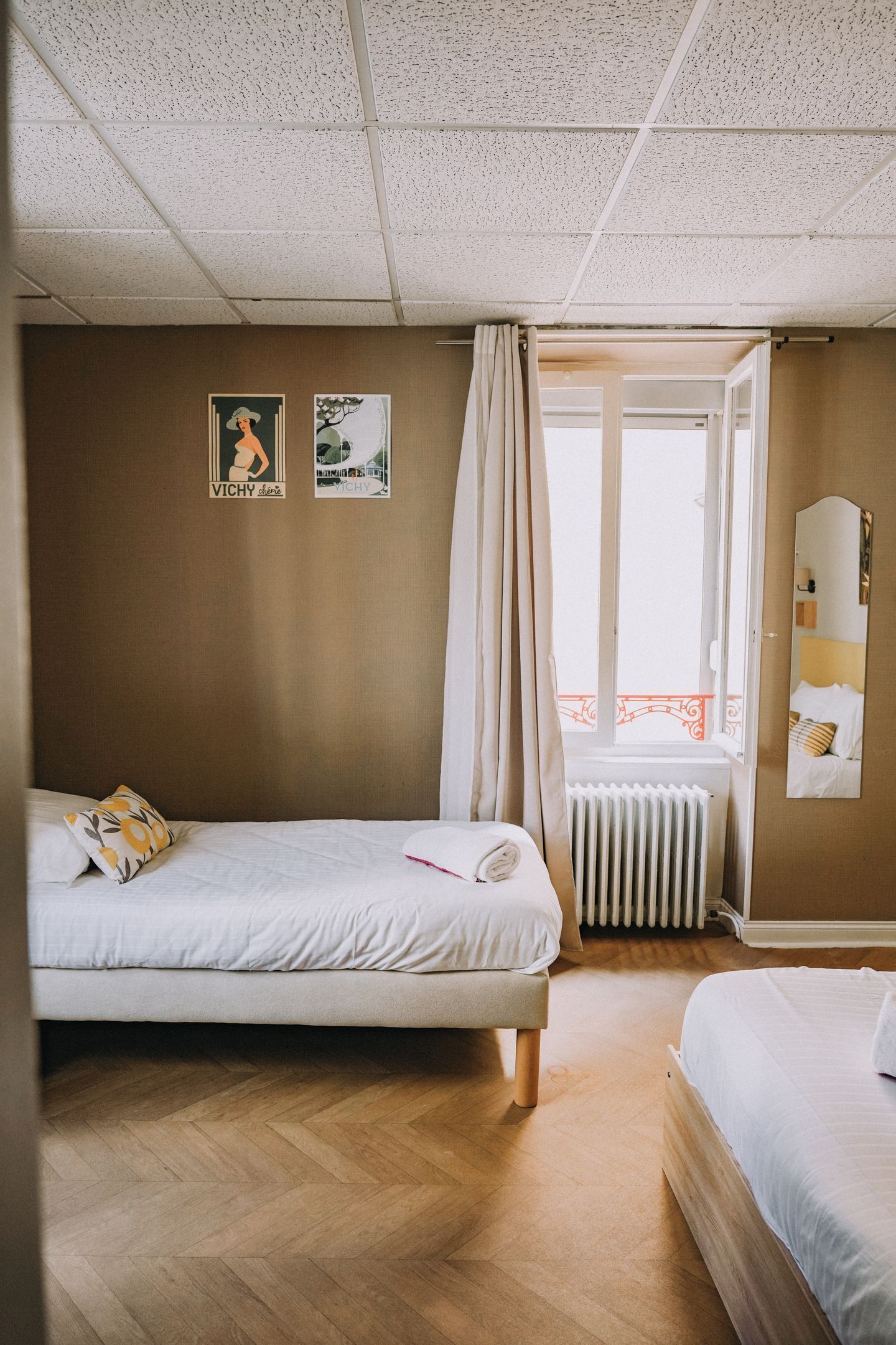 Una habitación de hotel con dos camas, un radiador, una ventana con cortinas y dos carteles en la pared.