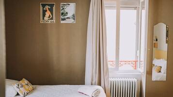 Una habitación de hotel con dos camas, un radiador, una ventana con cortinas y dos carteles en la pared.