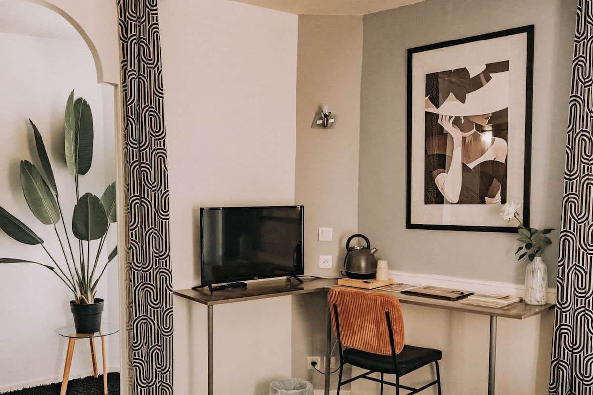 Habitación de hotel con cama, escritorio con televisor, silla, planta en maceta y un cuadro en la pared.