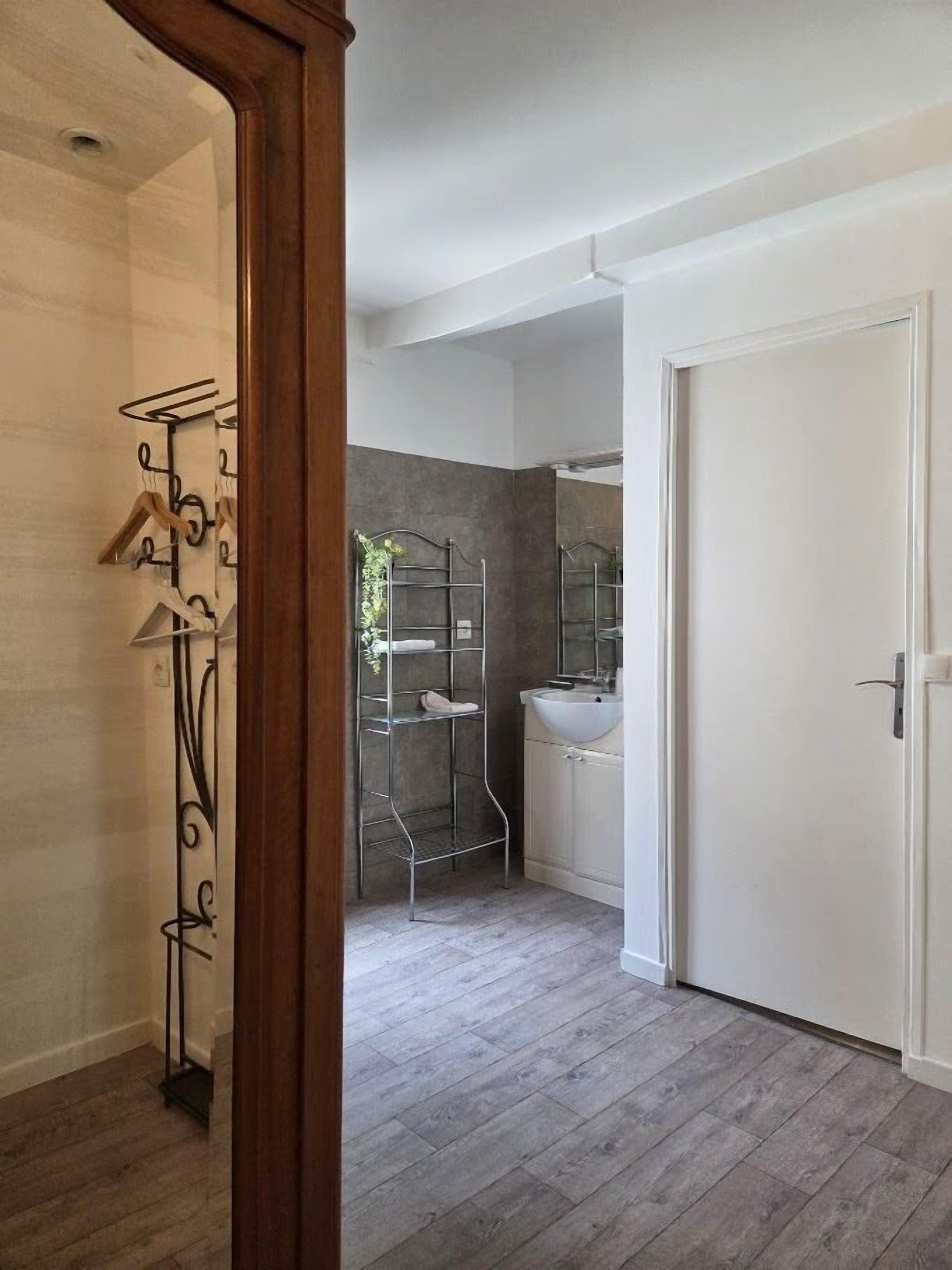 A modern bathroom with a grey tiled wall, a white sink, and a metal shower enclosure.