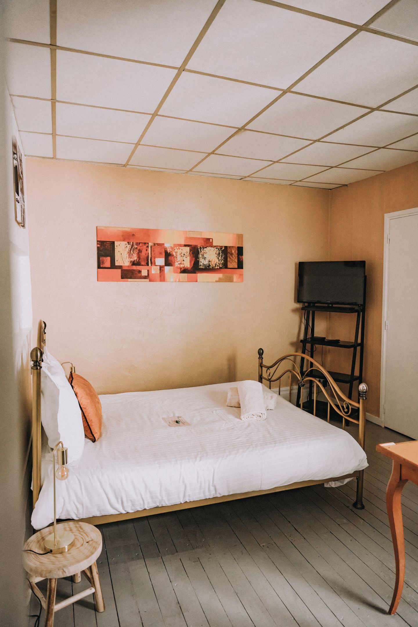 A bedroom with a bed, a television on a stand, and a painting on the wall.