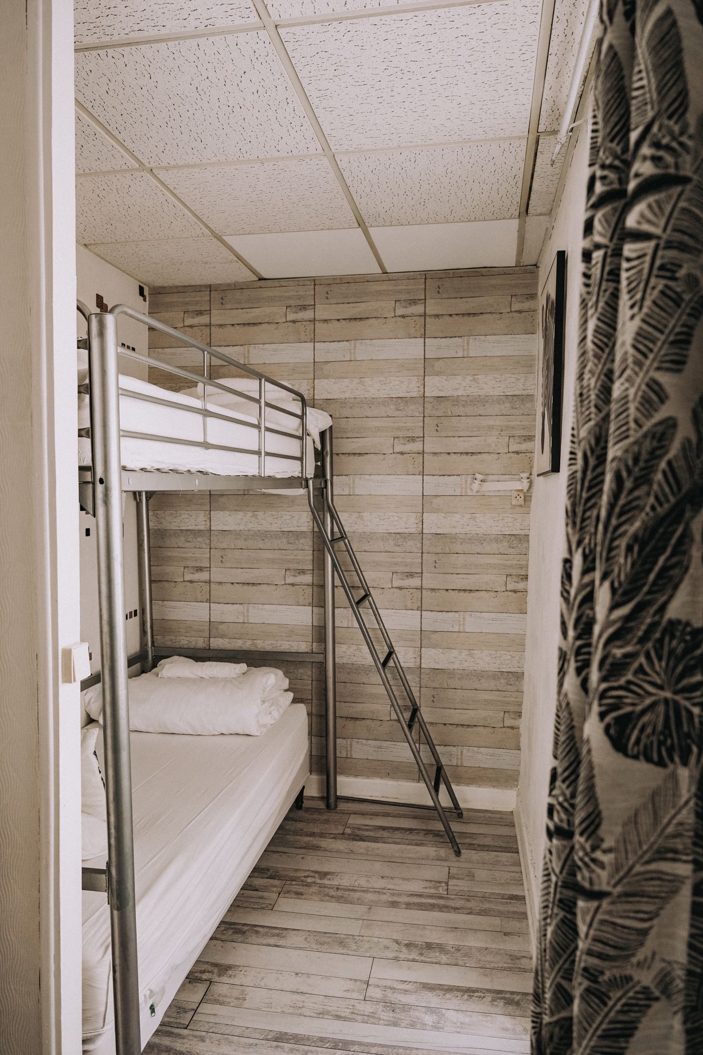 Habitación con literas, una pared de madera, una escalera y una cortina con estampado de hojas.