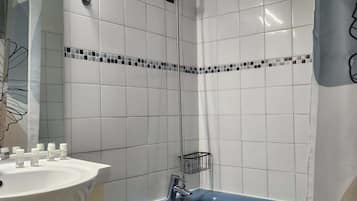 A bathroom with white tiled walls, a blue bathtub, a white sink with toiletries, and a shower head.