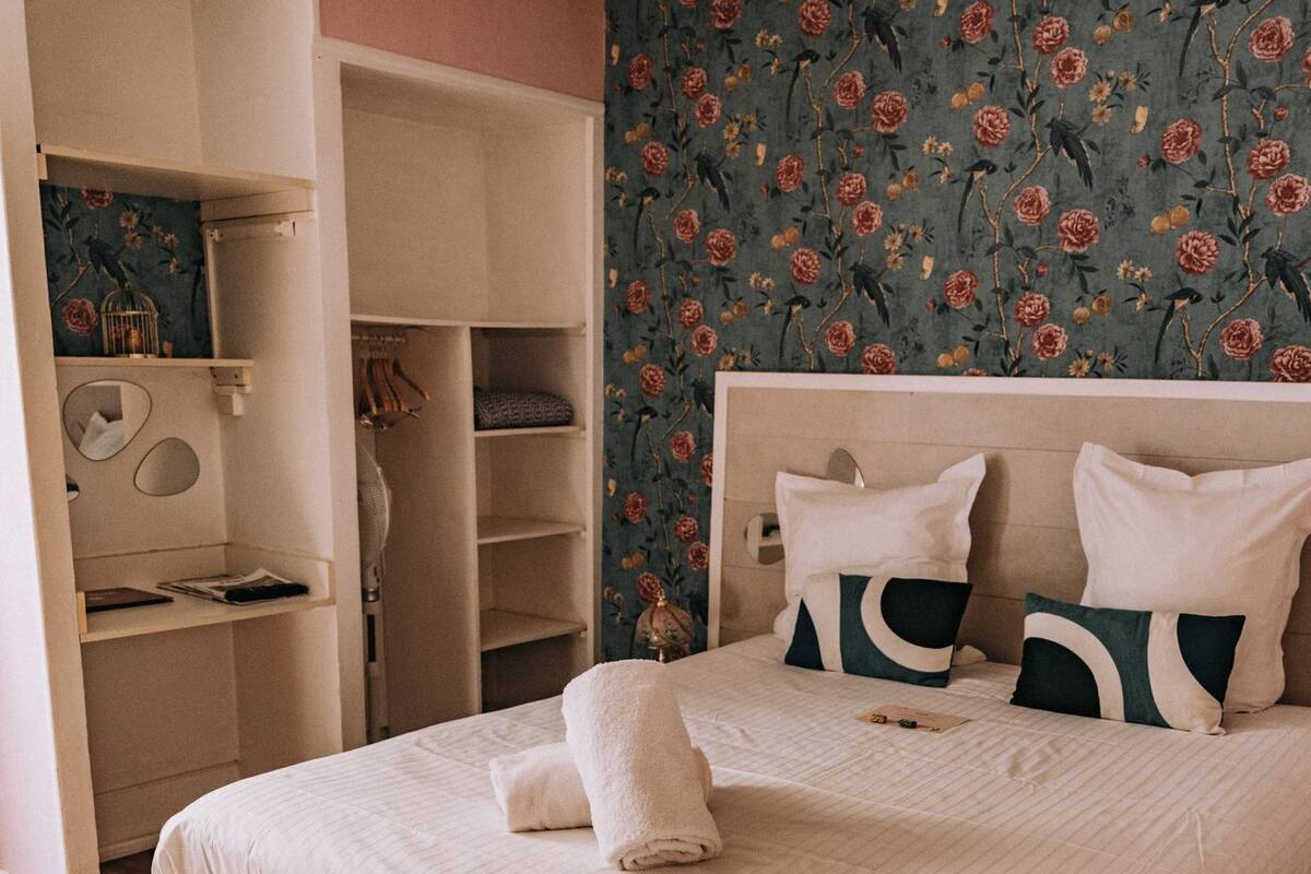 Un dormitorio con cama, armario y papel tapiz con motivos florales.
