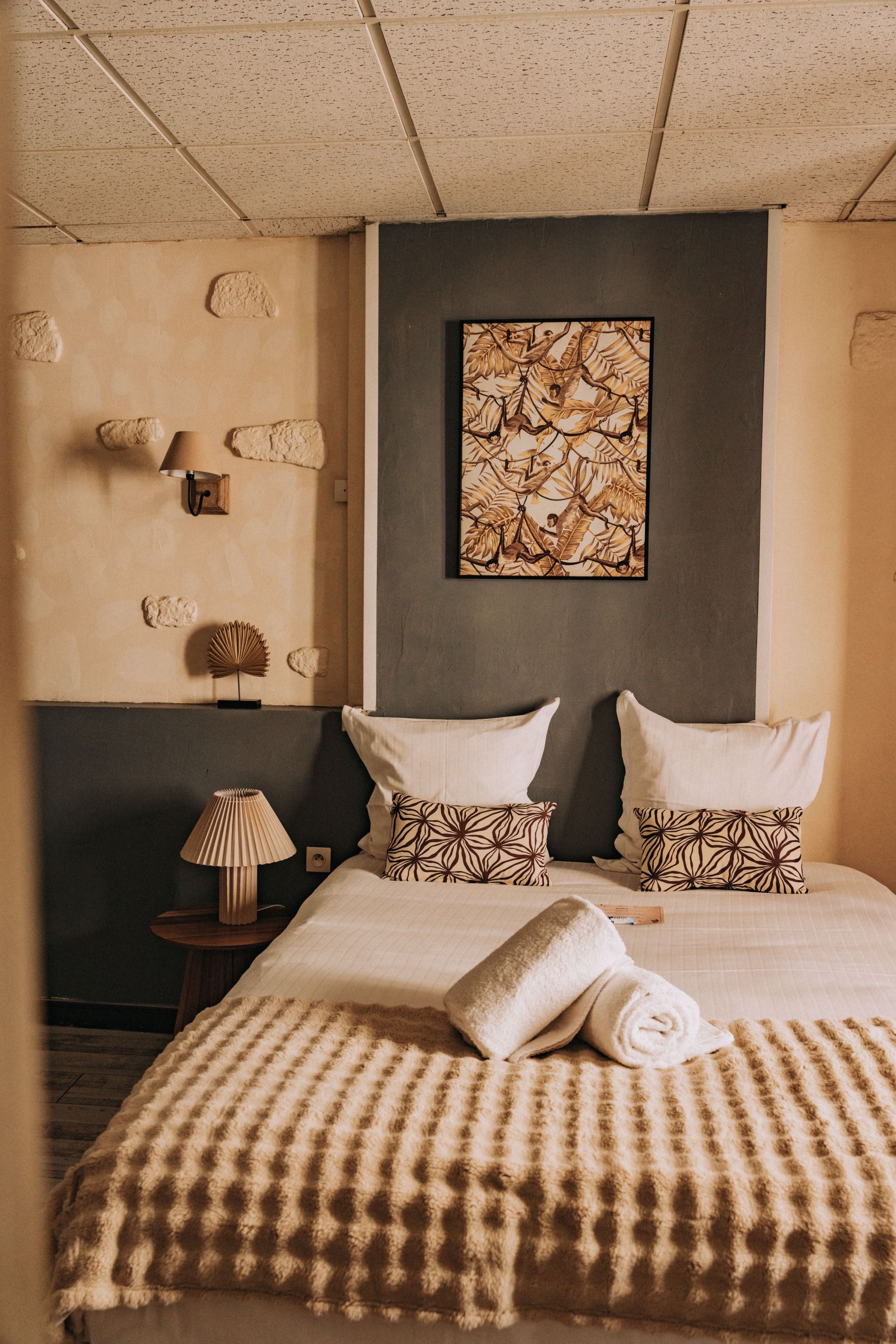 A hotel room with a bed, pillows, a wall-mounted artwork, a lamp, and a small table.