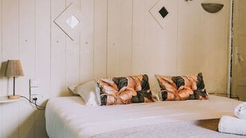 A bedroom with a bed, pillows, a lamp, and a wall with geometric patterns.