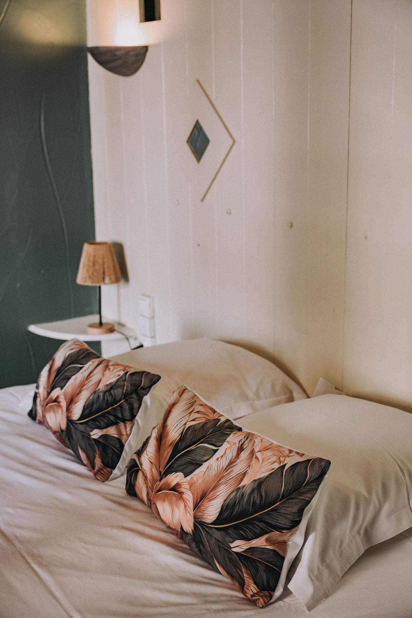 Una cama con almohadas estampadas con motivos florales, una lámpara de noche y una lámpara de pared.