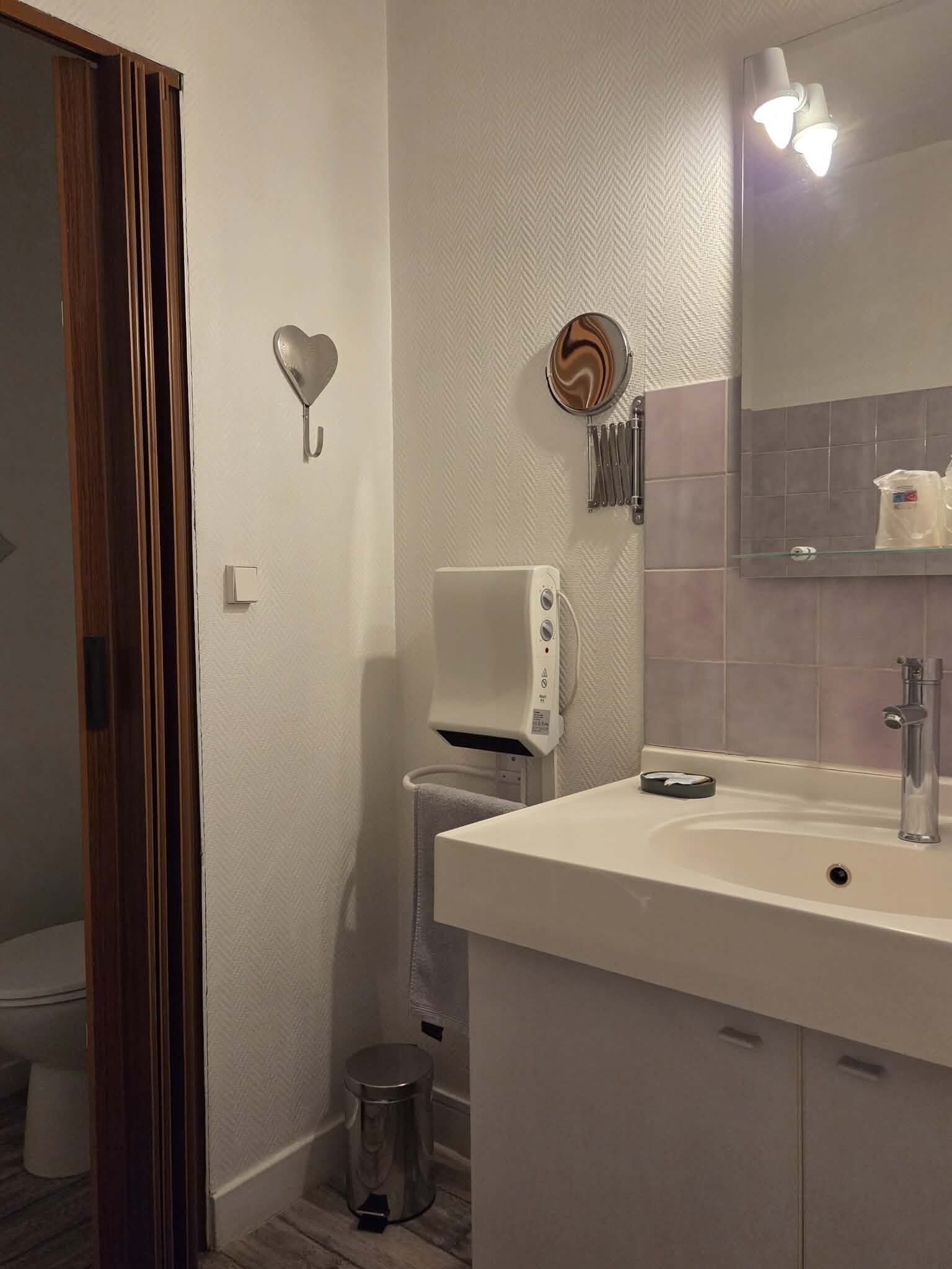 Une salle de bain avec un lavabo blanc, un miroir, un distributeur de savon et une poubelle.