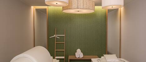 A modern bedroom with a green accent wall, two white beds, a wooden bench with towels, and a ladder.