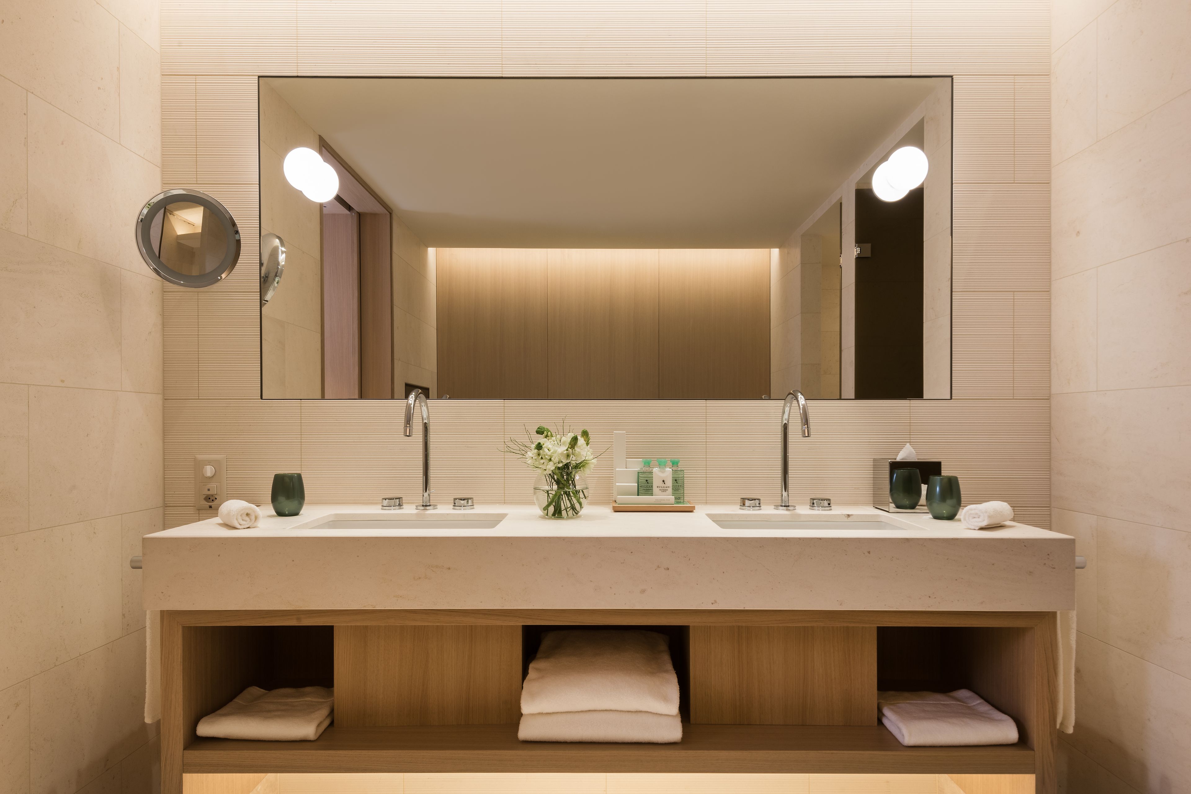 Un baño moderno con un espejo grande, dos lavamanos y estantes empotrados para toallas.