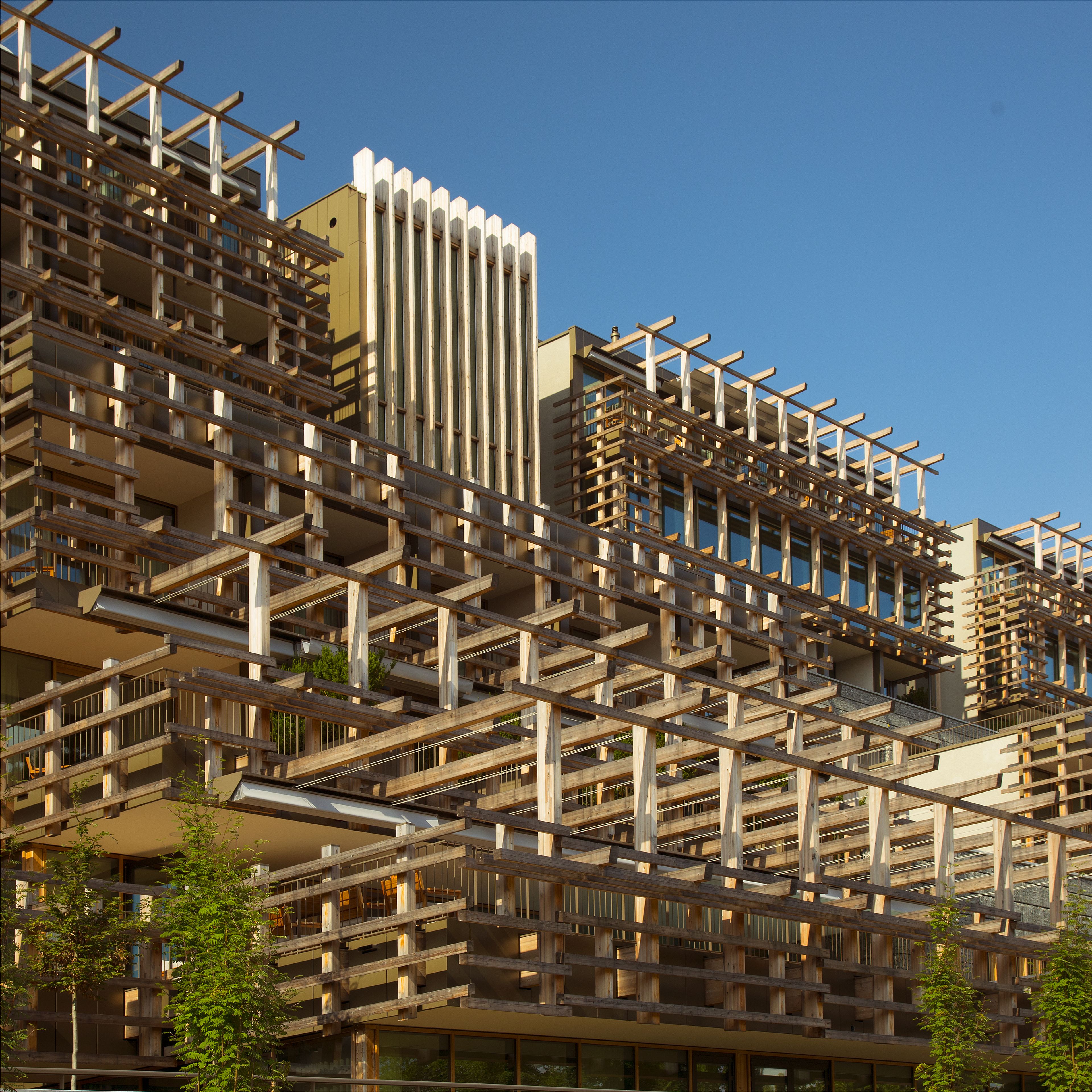 Een modern hoog gebouw met een unieke houten gevel en meerdere balkons.