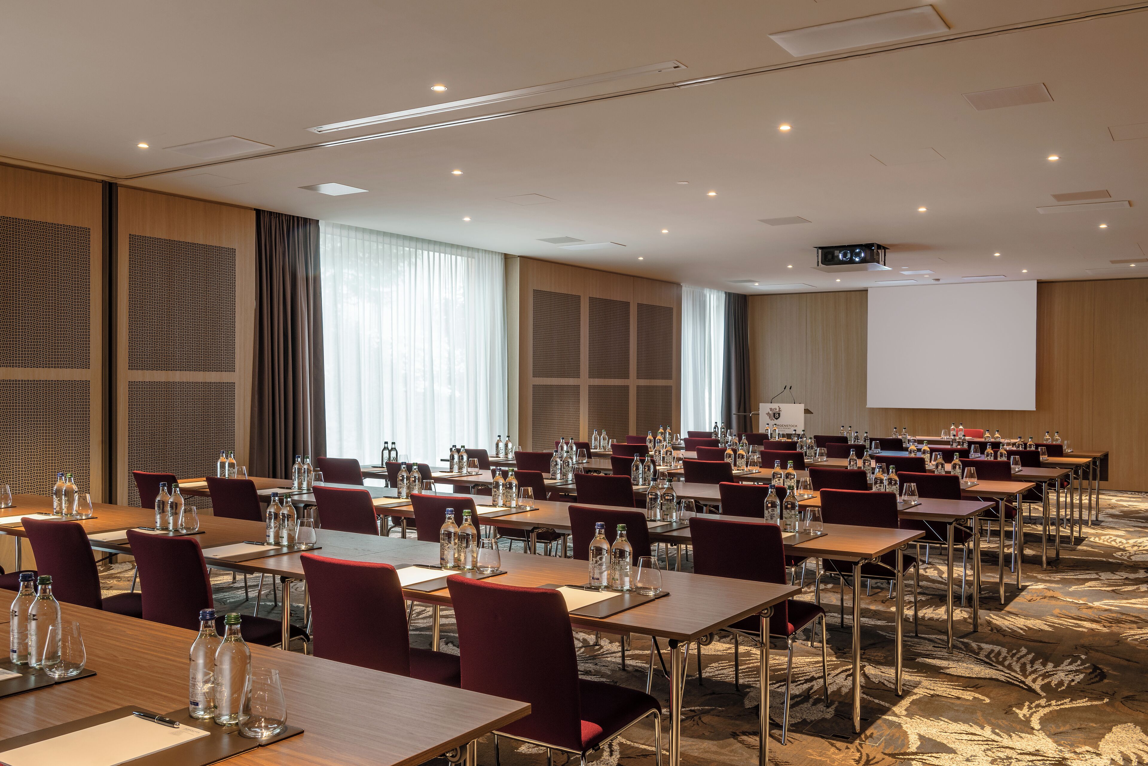Un salón de conferencias con varias mesas, sillas y una pantalla de proyector.