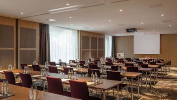 Un salón de conferencias con varias mesas, sillas y una pantalla de proyector.
