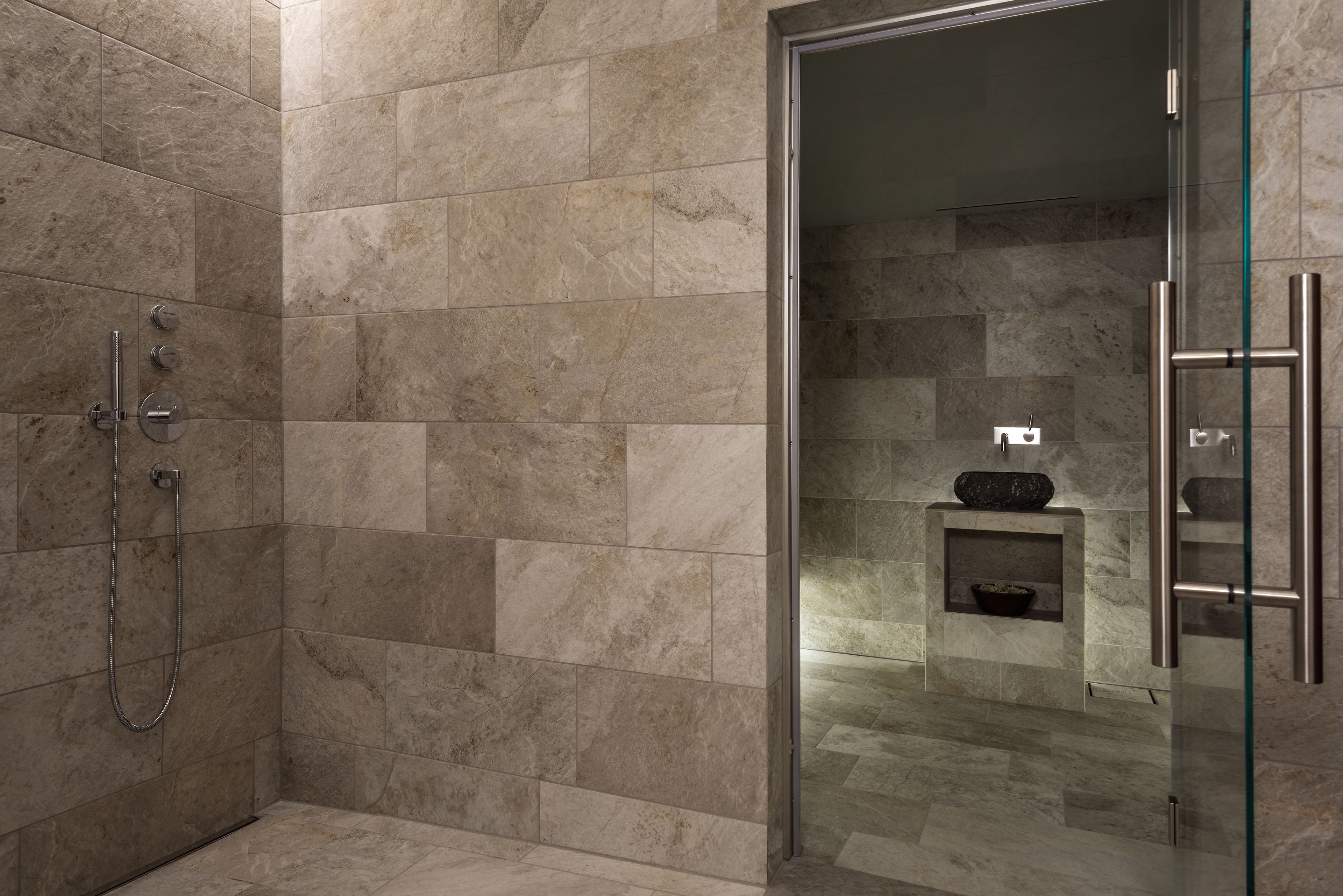A modern bathroom with a glass shower enclosure, marble tiles, and a built-in sink with a stone basin.