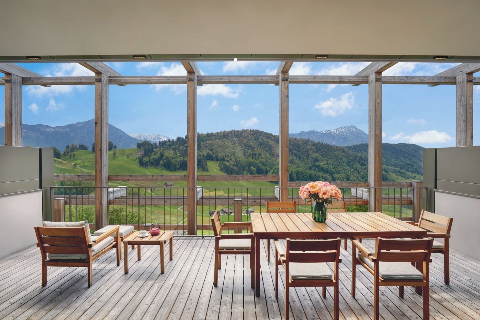 A wooden deck with a table and chairs, overlooking a mountainous landscape.