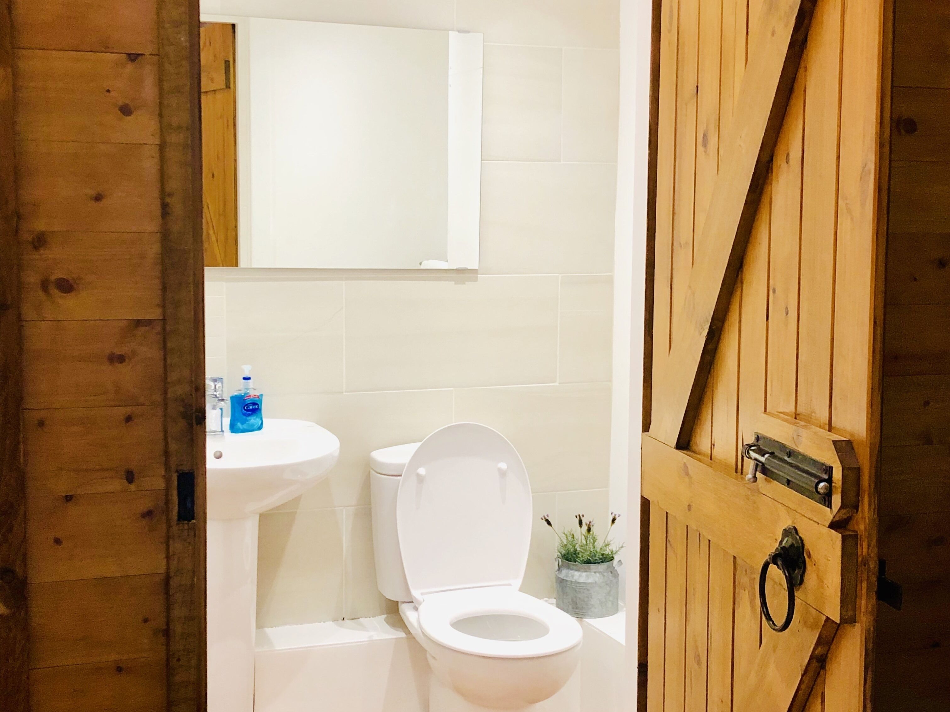 Un baño con puerta de madera, un lavabo blanco, un inodoro y un espejo sobre el lavabo.