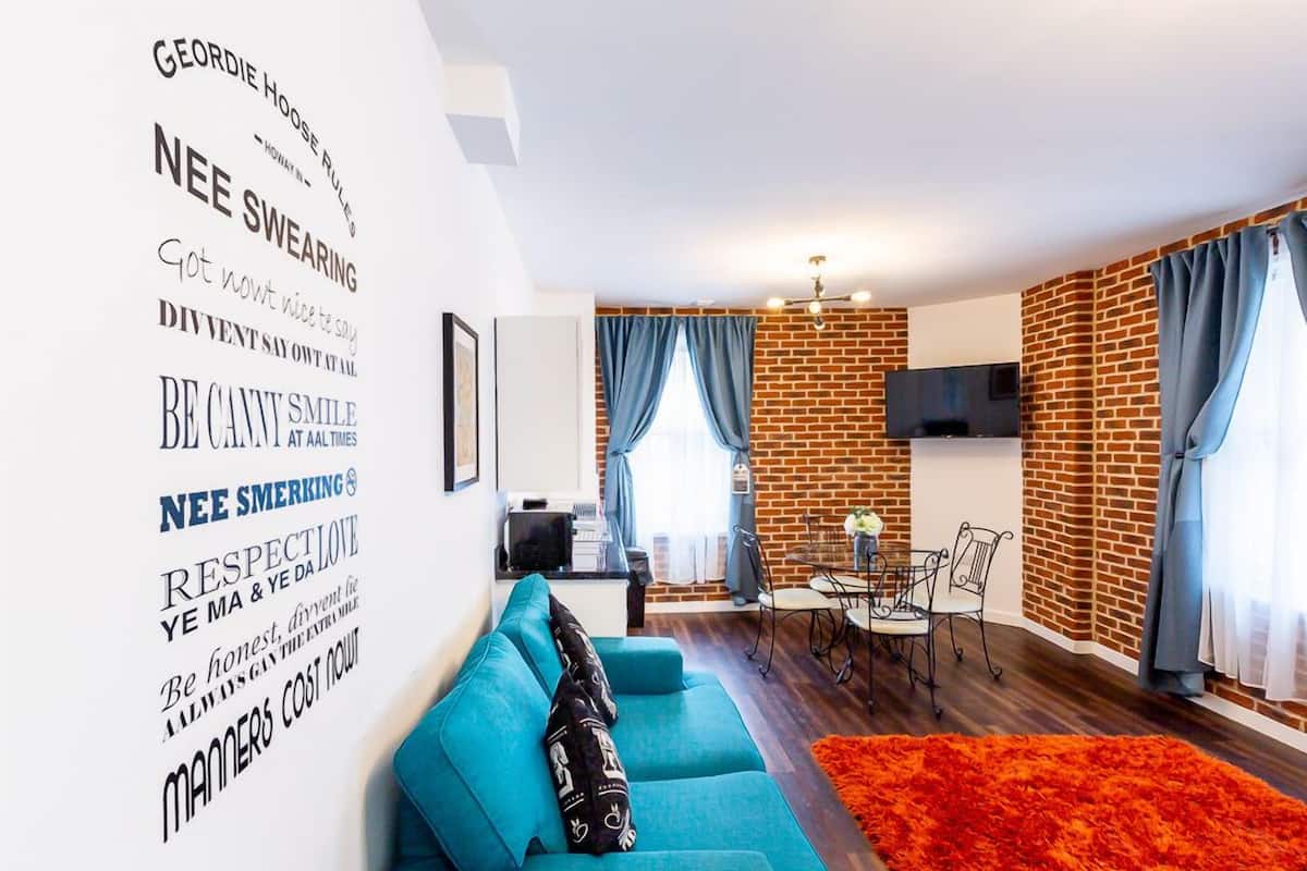 A modern living room with a blue sofa, a red rug, and a brick wall.