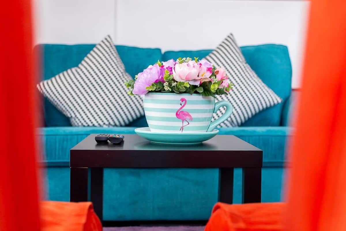 A teal sofa with striped pillows, a teal and white striped mug with a flamingo design, and a small black table with a remote control.