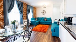 A modern living room with a blue sofa, a glass dining table, and a kitchen area with a microwave. - Honeypot House (Newcastle-upon-Tyne)