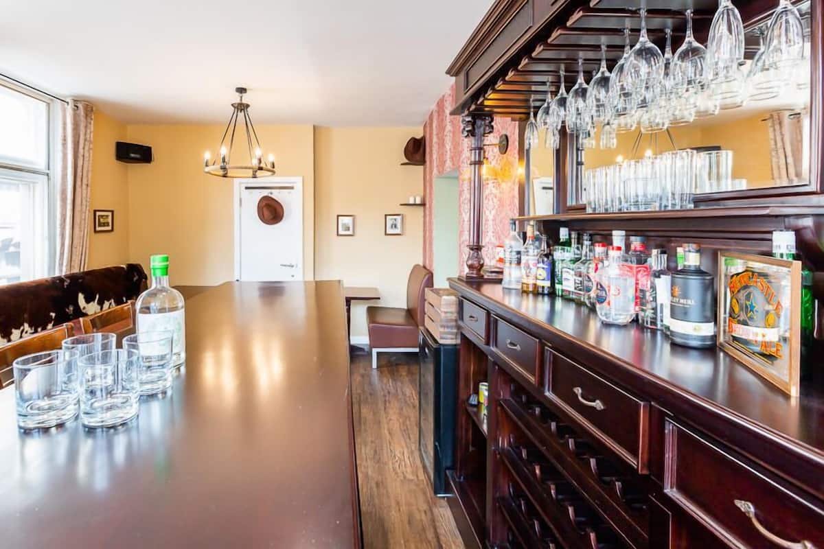 A bar area with a long counter, glasses, bottles, and a hanging wine rack.