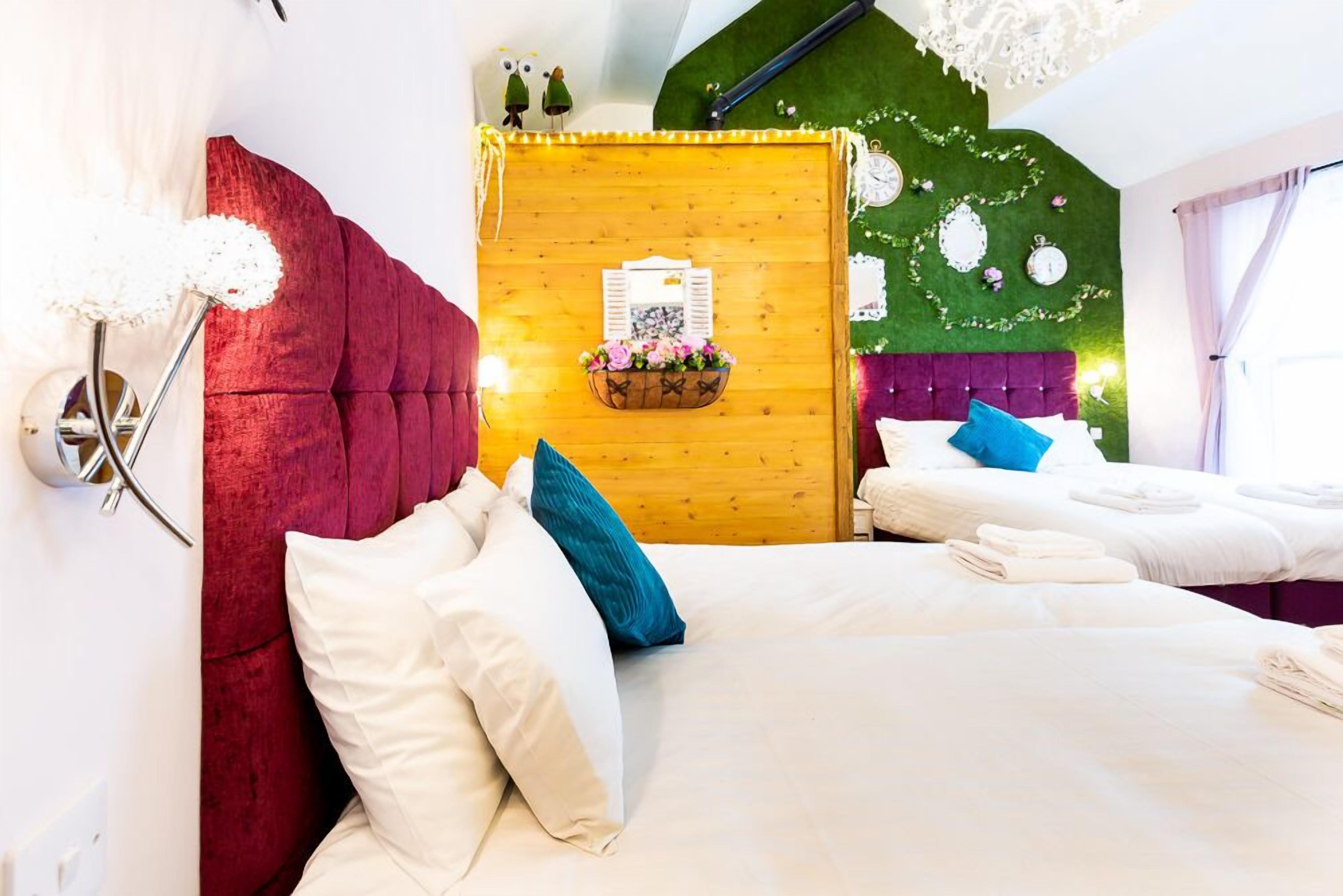 Habitación de hotel con dos camas, cabecera roja, panel de pared de madera y pared verde con un reloj y elementos decorativos.