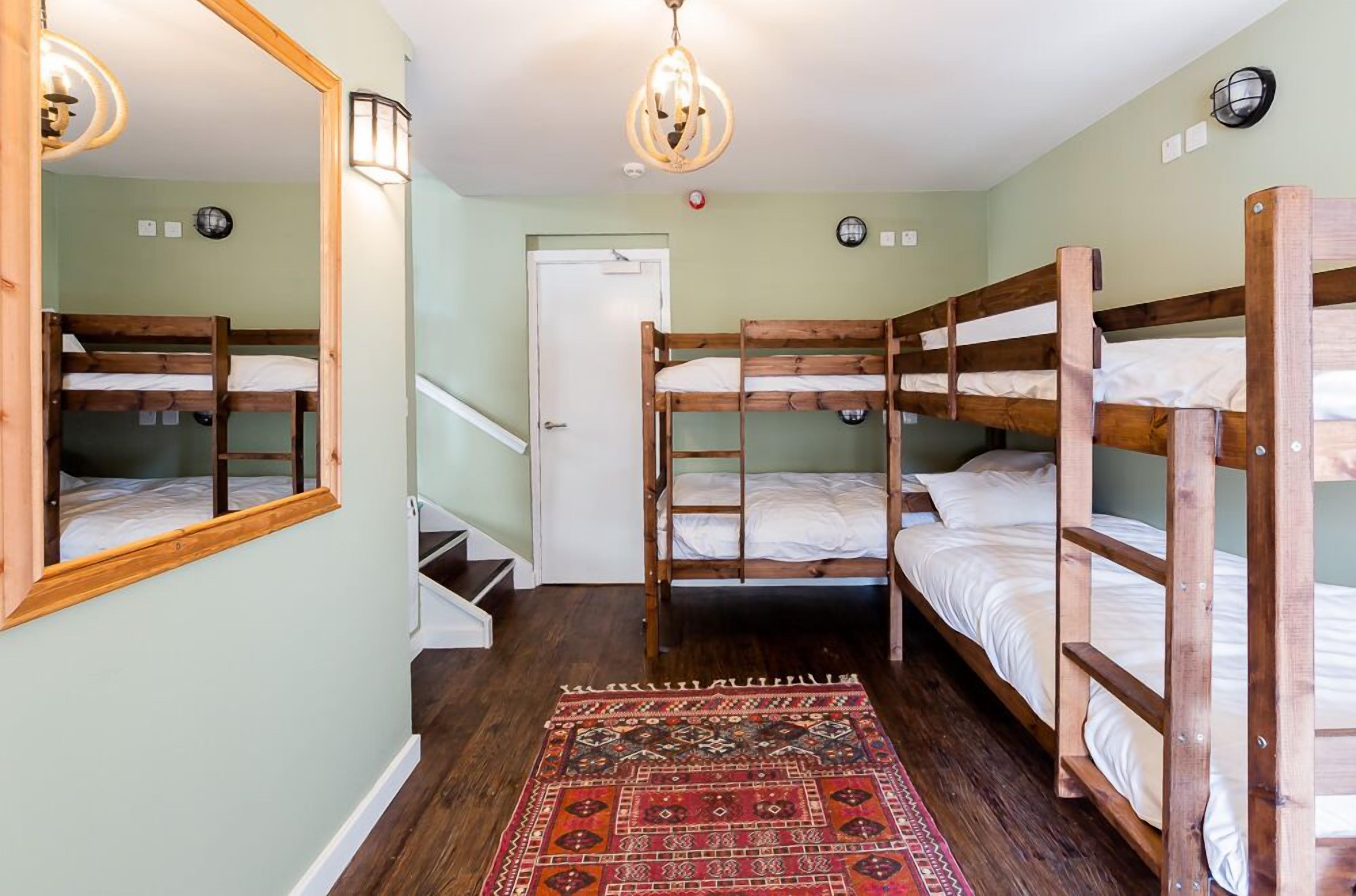 Una habitación con literas, suelo de madera, alfombra estampada y candelabro.