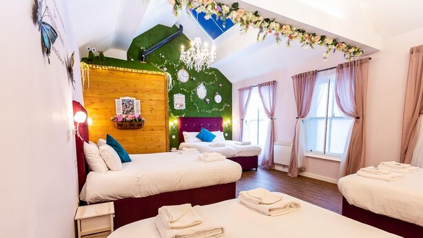A hotel room with two beds, a green wall, a chandelier, and a window with curtains. - Honeypot House (Newcastle-upon-Tyne)