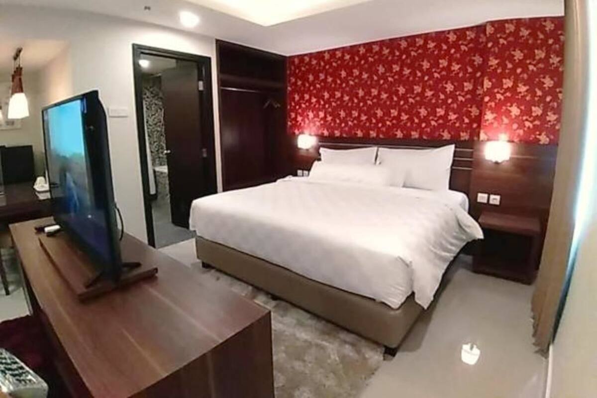 A modern bedroom with a large bed, a TV on a wooden stand, and a red floral wallpaper.