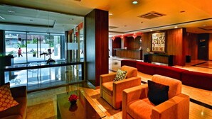 A modern lobby with a glass entrance, red seating area, and a reception desk. - CoreHotel Malioboro City Yogyakarta (Depok)