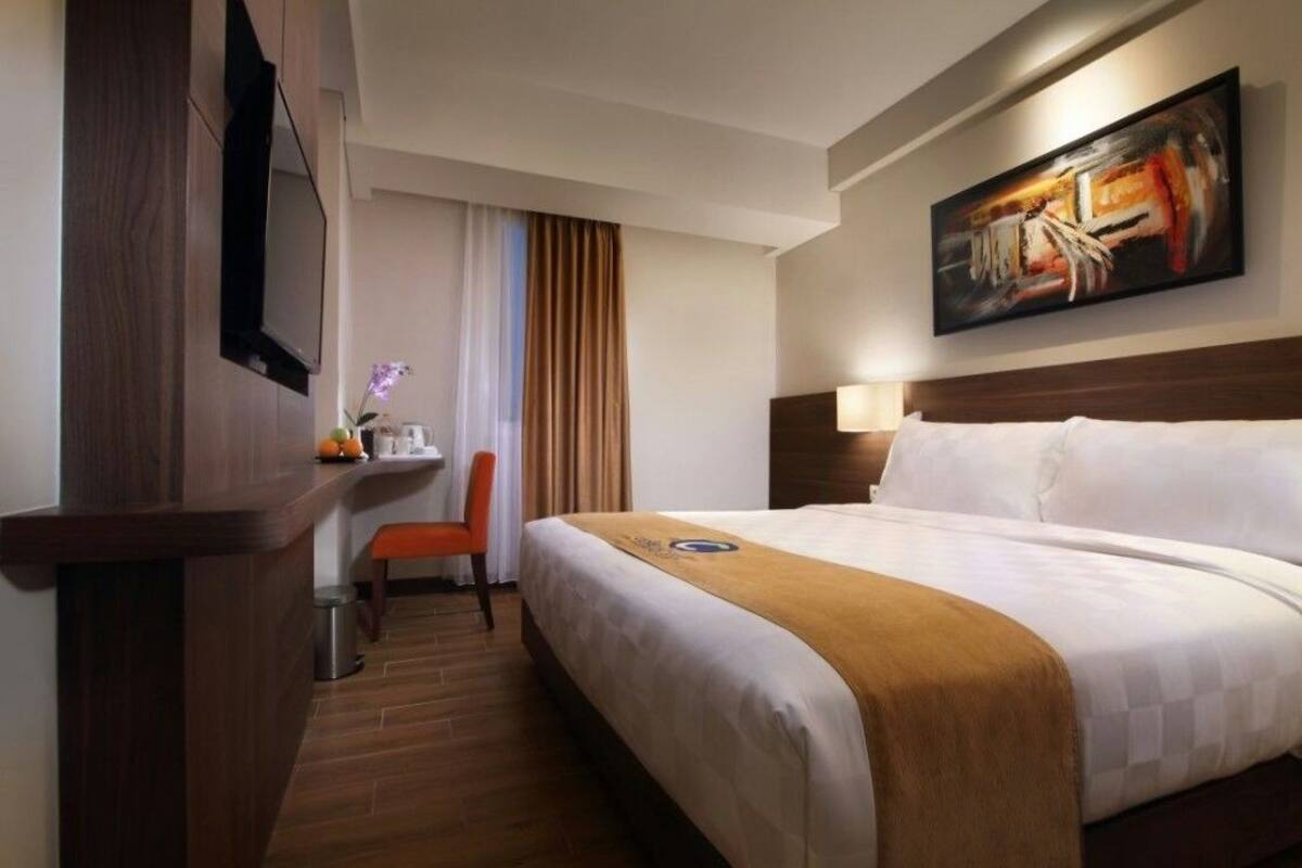 A hotel room with a bed, a desk, a chair, and a painting on the wall.
