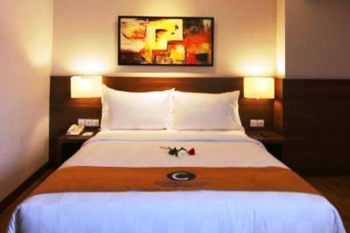 A hotel room with a large bed, two bedside tables, a wall-mounted painting, and a wooden headboard.