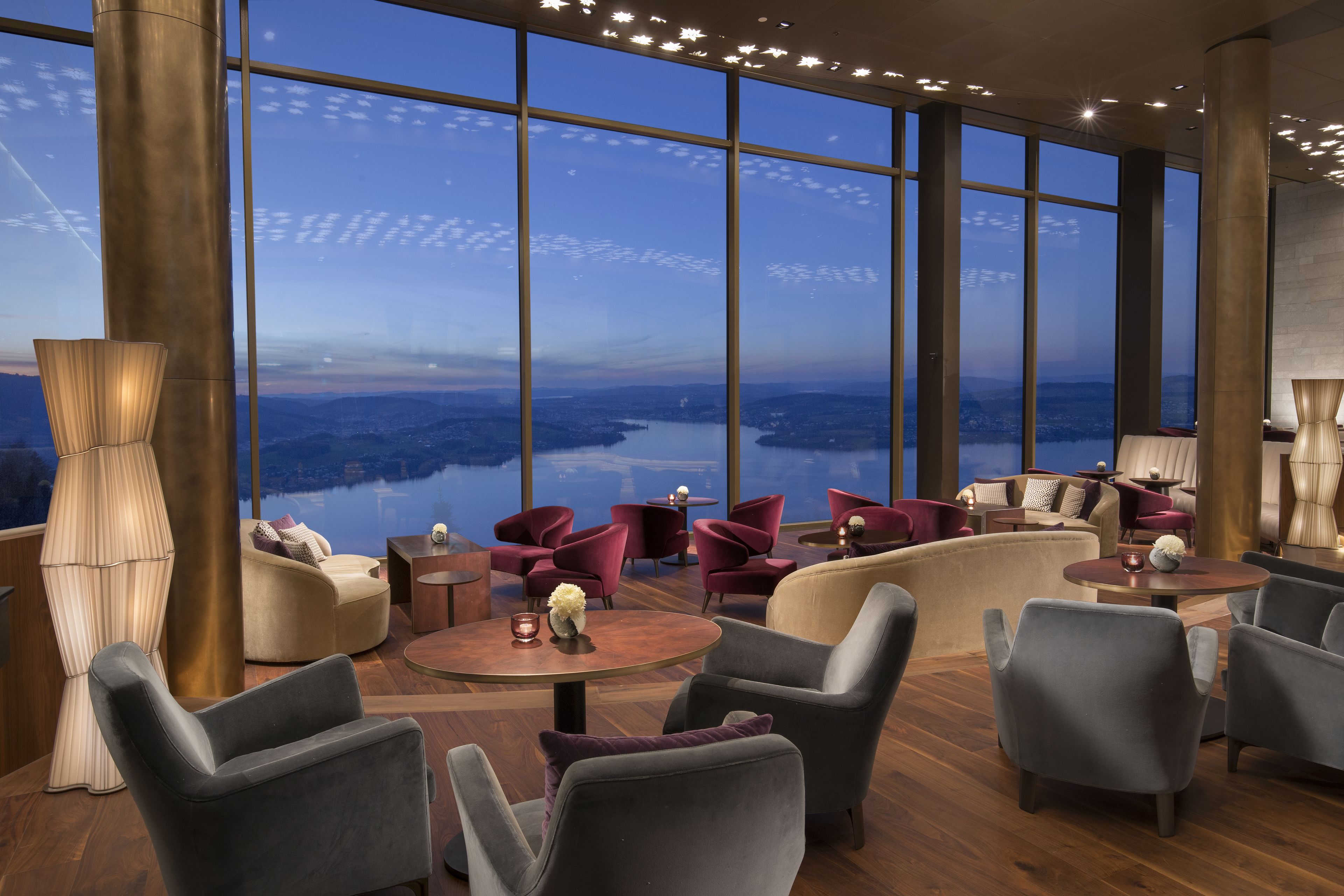 A modern lounge with large windows offering a view of a lake and mountains.