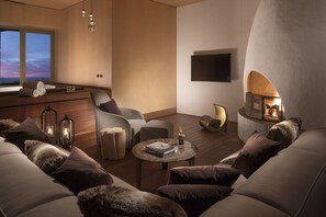 A modern living room with a fireplace, comfortable seating, and a view of the sky through a large window.