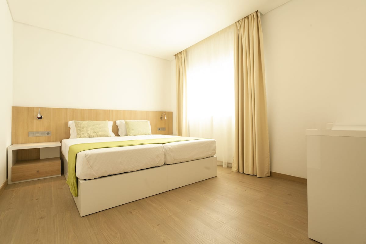 A hotel room with a bed, bedside table, and a window with curtains.