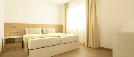 A hotel room with a bed, bedside table, and a window with curtains.