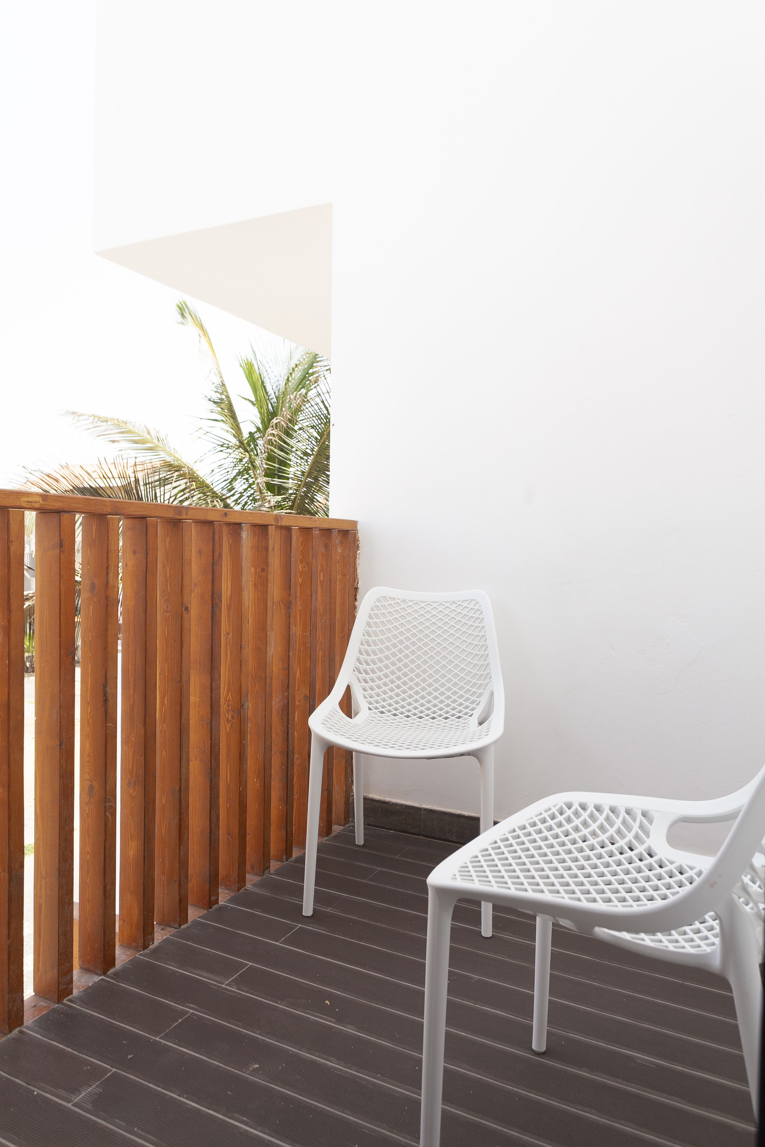 A balcony with a wooden fence, two white plastic chairs, and a palm tree in the background.