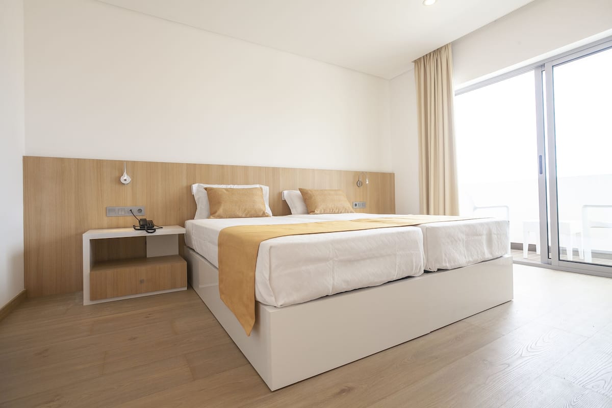 A modern hotel room with a large bed, a bedside table, and a view through a sliding glass door.