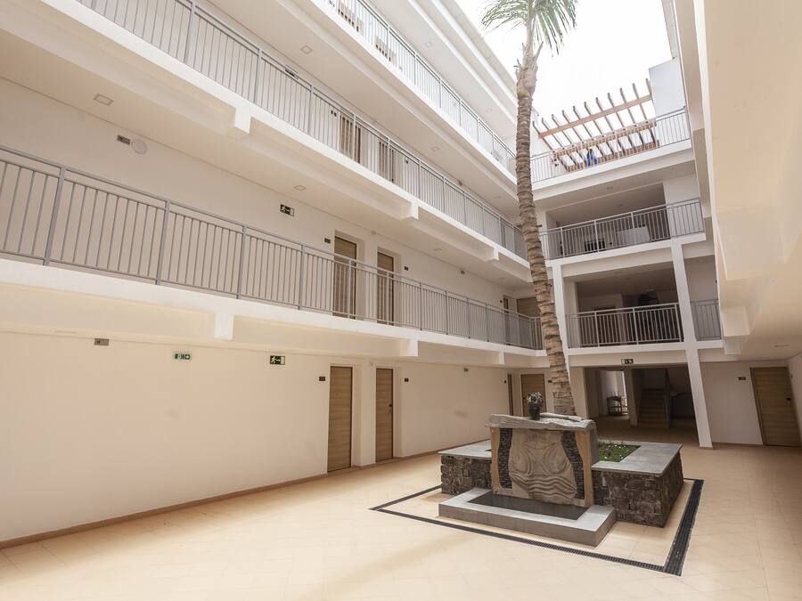 A multi-level atrium with a central courtyard, featuring a palm tree, a decorative fountain, and a stone bench.