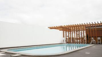 A pool area with a wooden pergola and white chairs.