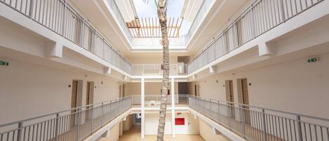 A multi-level atrium with a central palm tree, white railings, and a modern architectural design.
