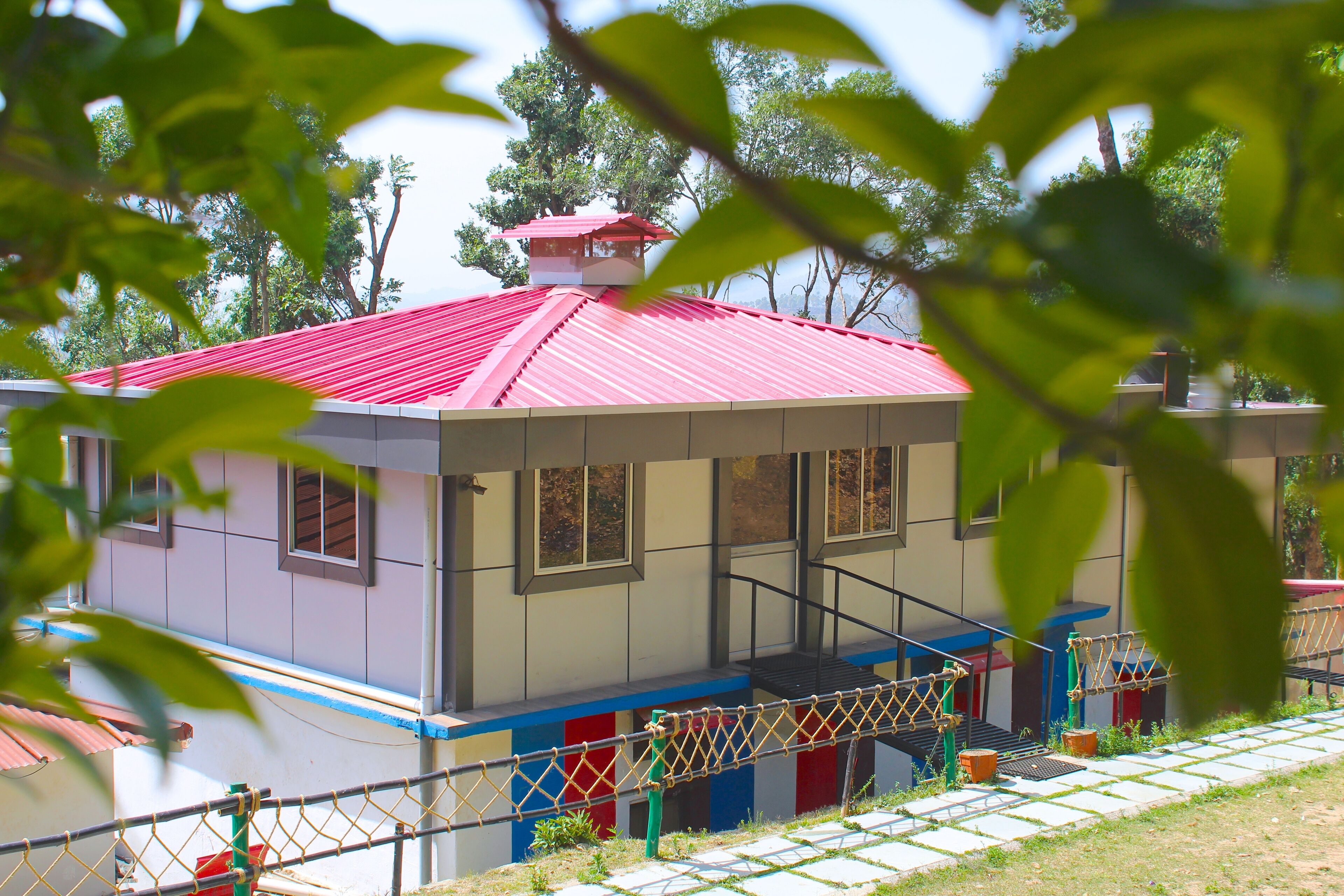 Un edificio con tejado rojo, un área cercada con elementos coloridos y una escalera que lleva a una plataforma.