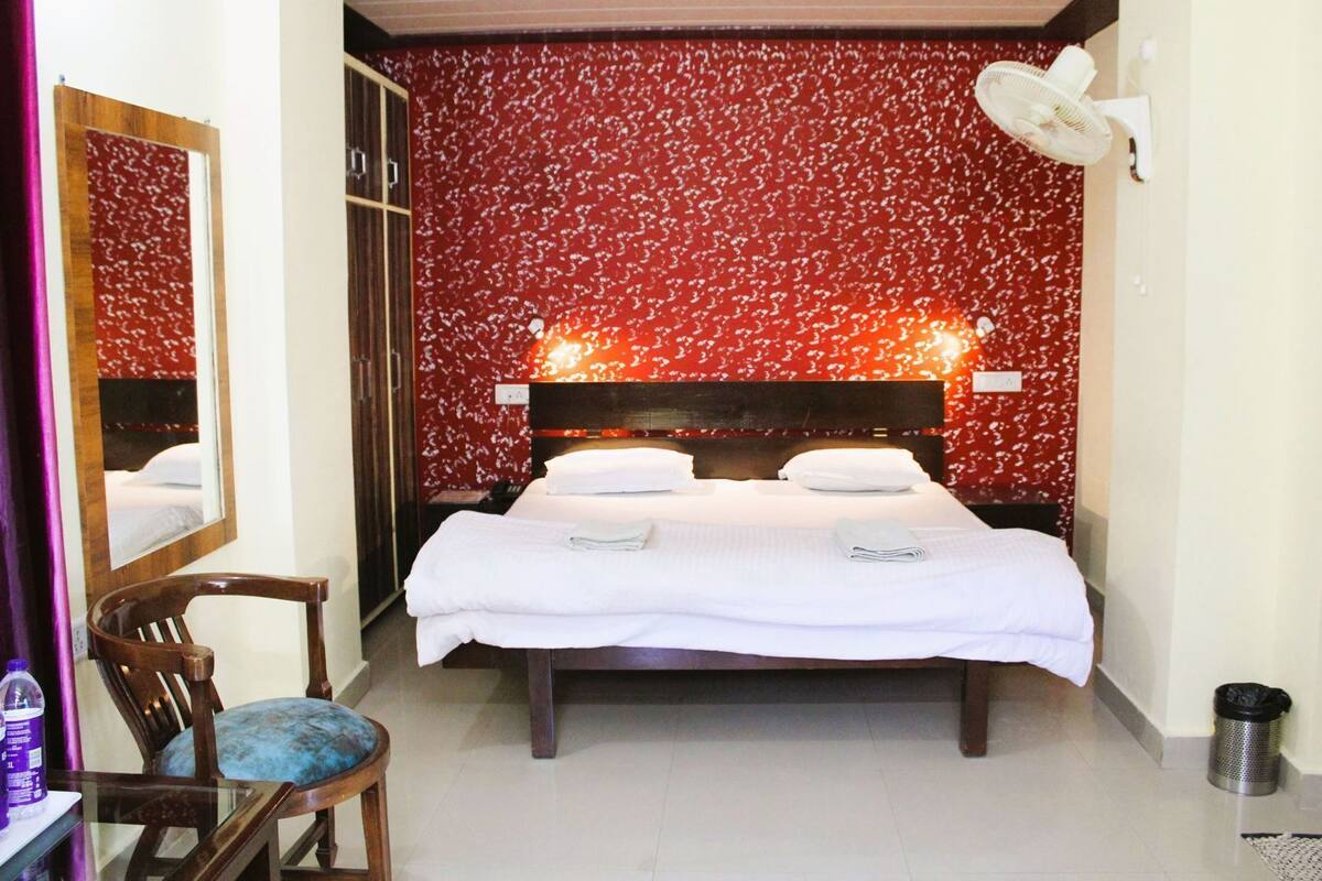 Una habitación de hotel con una cama, una silla, un espejo y un ventilador de pared.