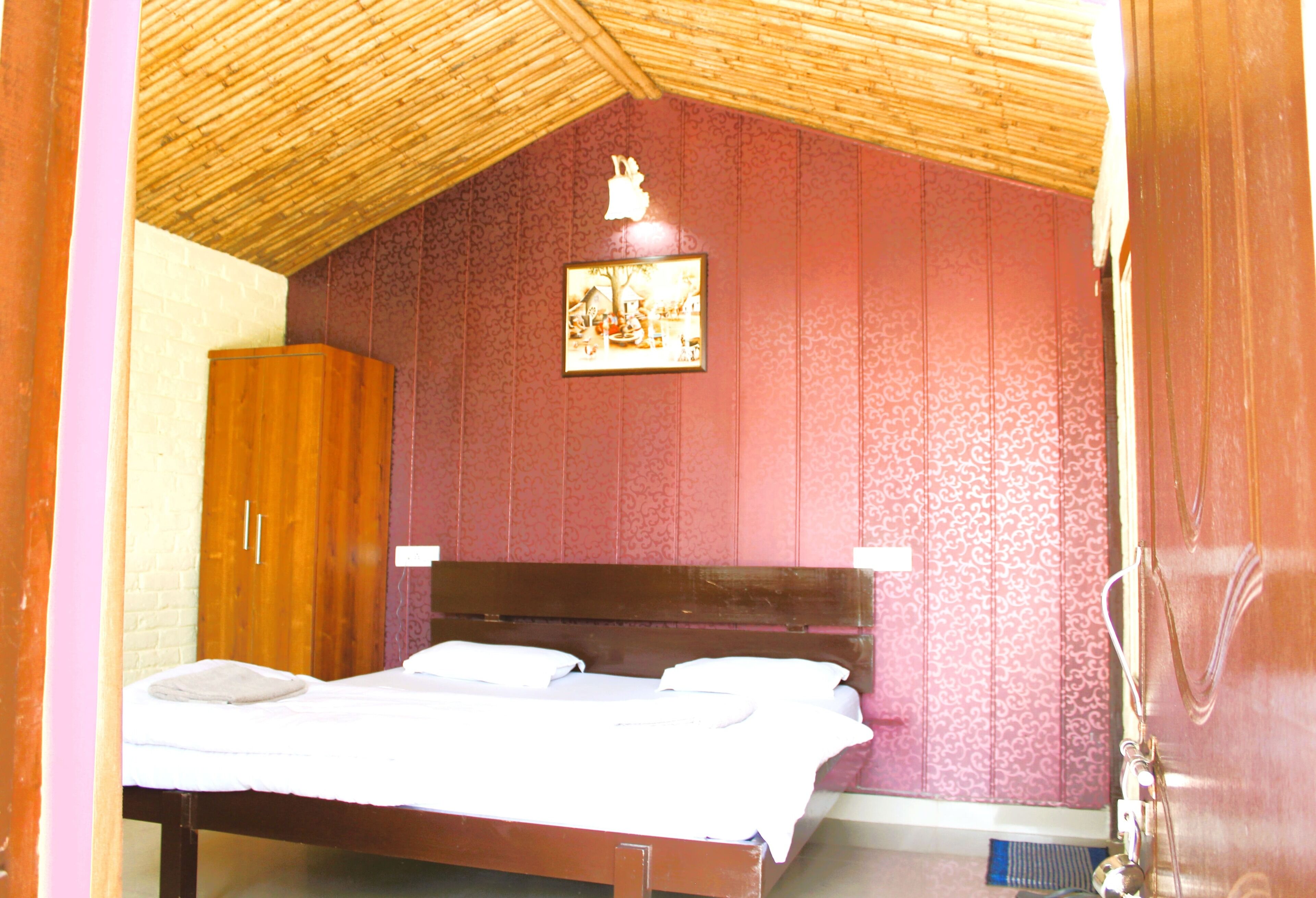 A bedroom with a wooden bed, a wooden wardrobe, and a wall-mounted picture.