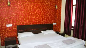 Habitación de hotel con una cama grande, dos almohadas, una mesita de noche, una pequeña mesa y una ventana con cortinas.