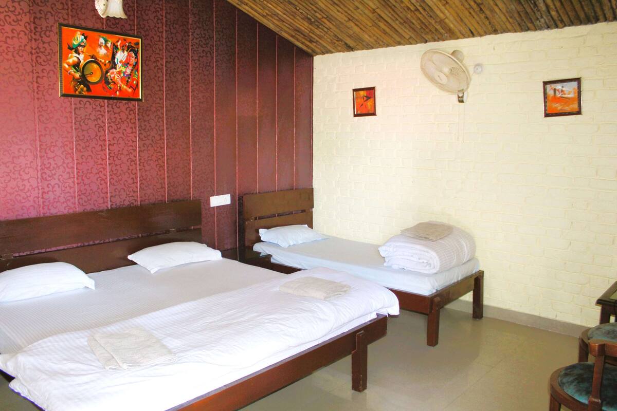 Una habitación de hotel con tres camas individuales, techo de madera y pared de ladrillo.