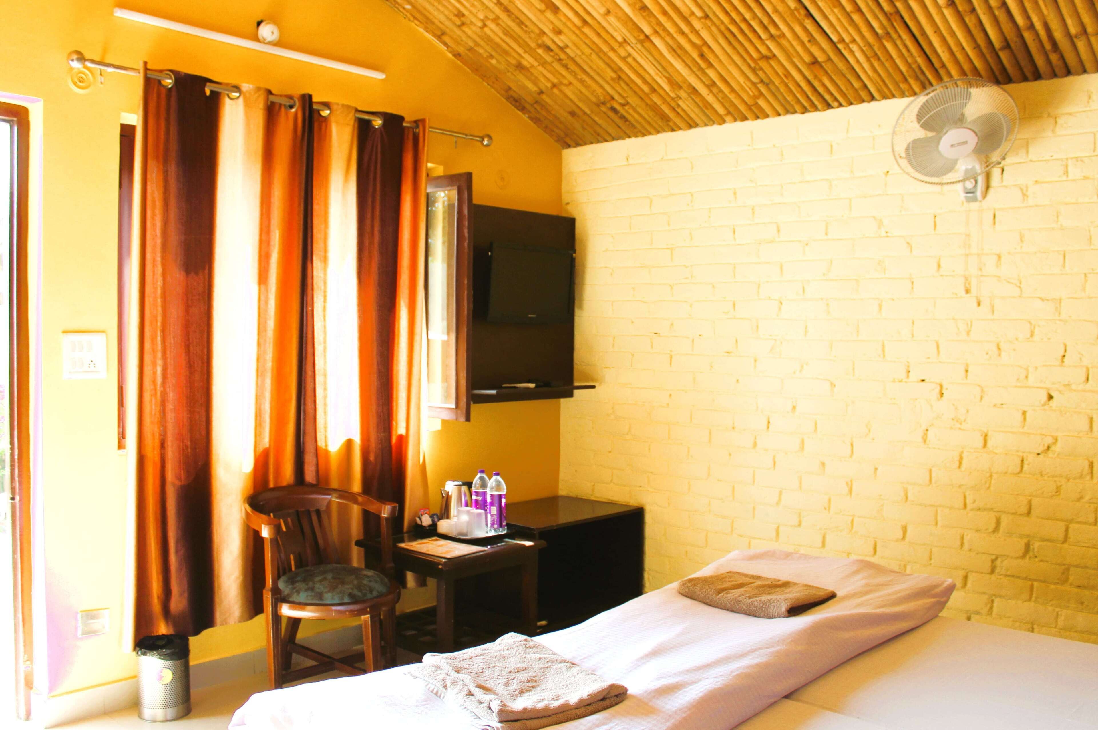 A room with a bed, a chair, a desk, a television, and a fan.