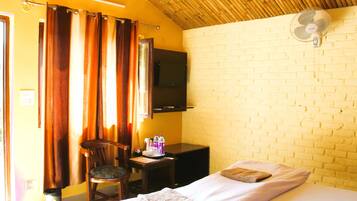 A room with a bed, a chair, a desk, a television, and a fan.