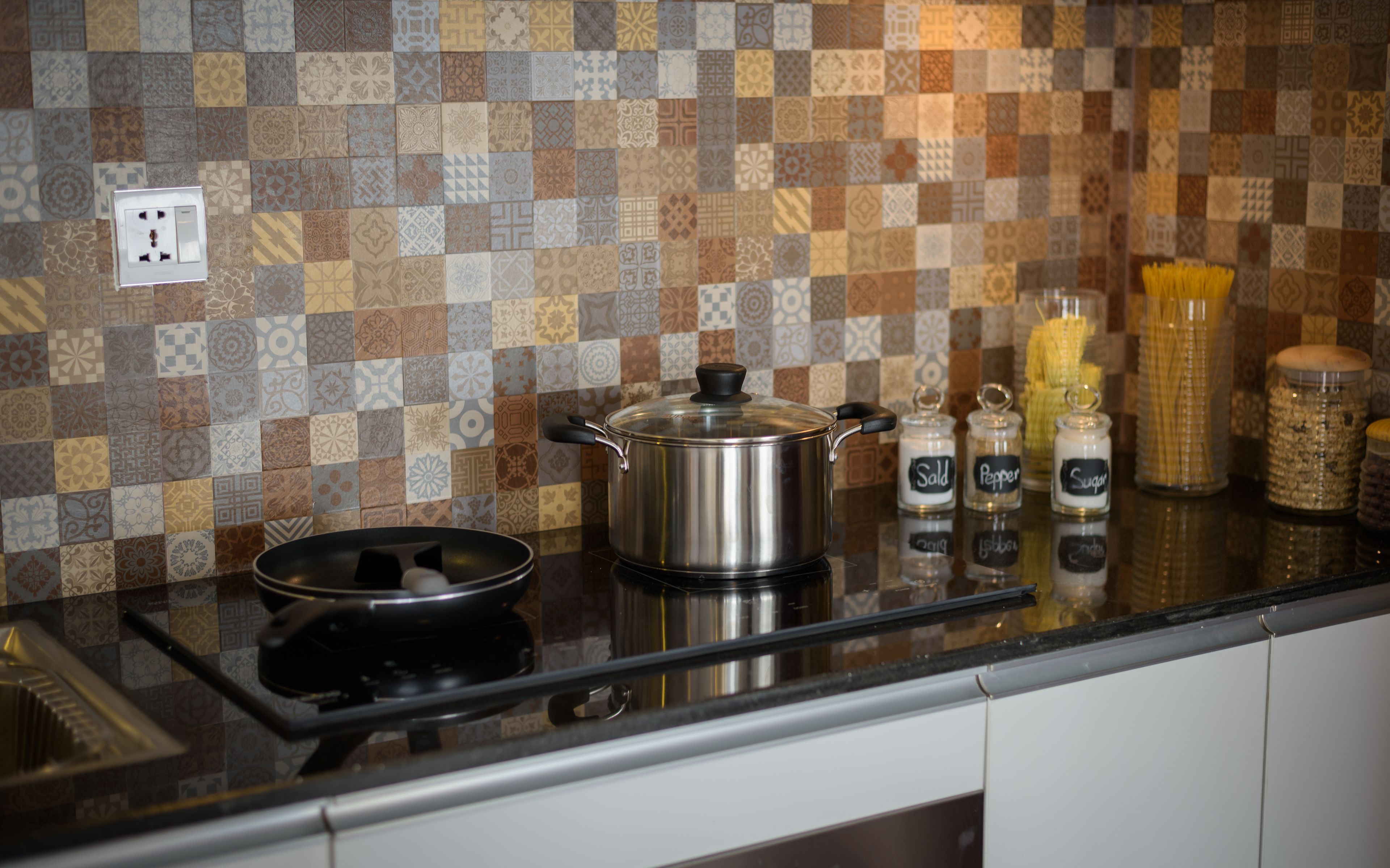 A kitchen with a checkered backsplash, a stainless steel pot on the counter, and spice jars labeled "Sald," "Pepper," and "Sugar."