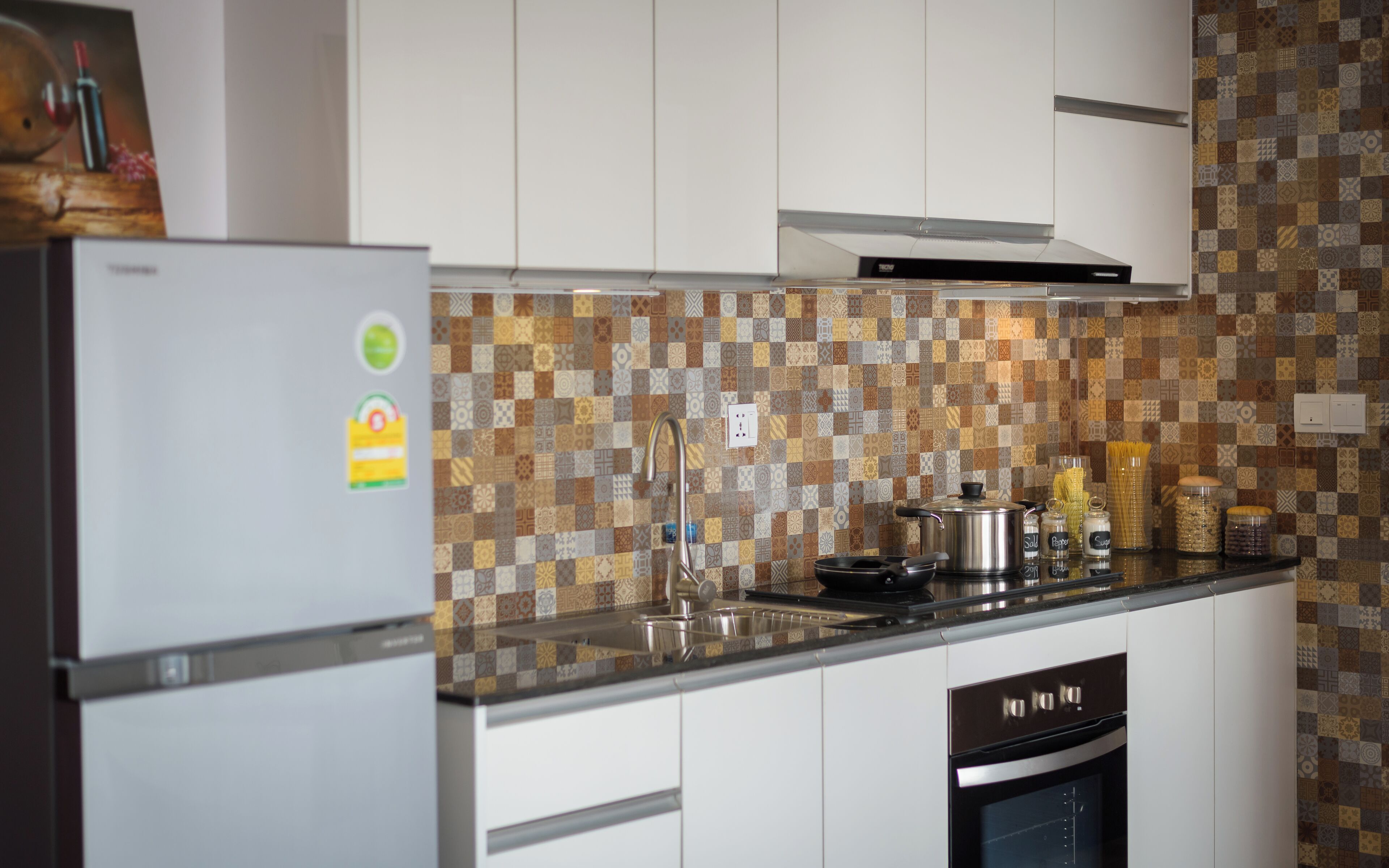 Una cucina moderna con mobili bianchi, un frigorifero in acciaio inox, un backsplash decorato e un forno integrato.
