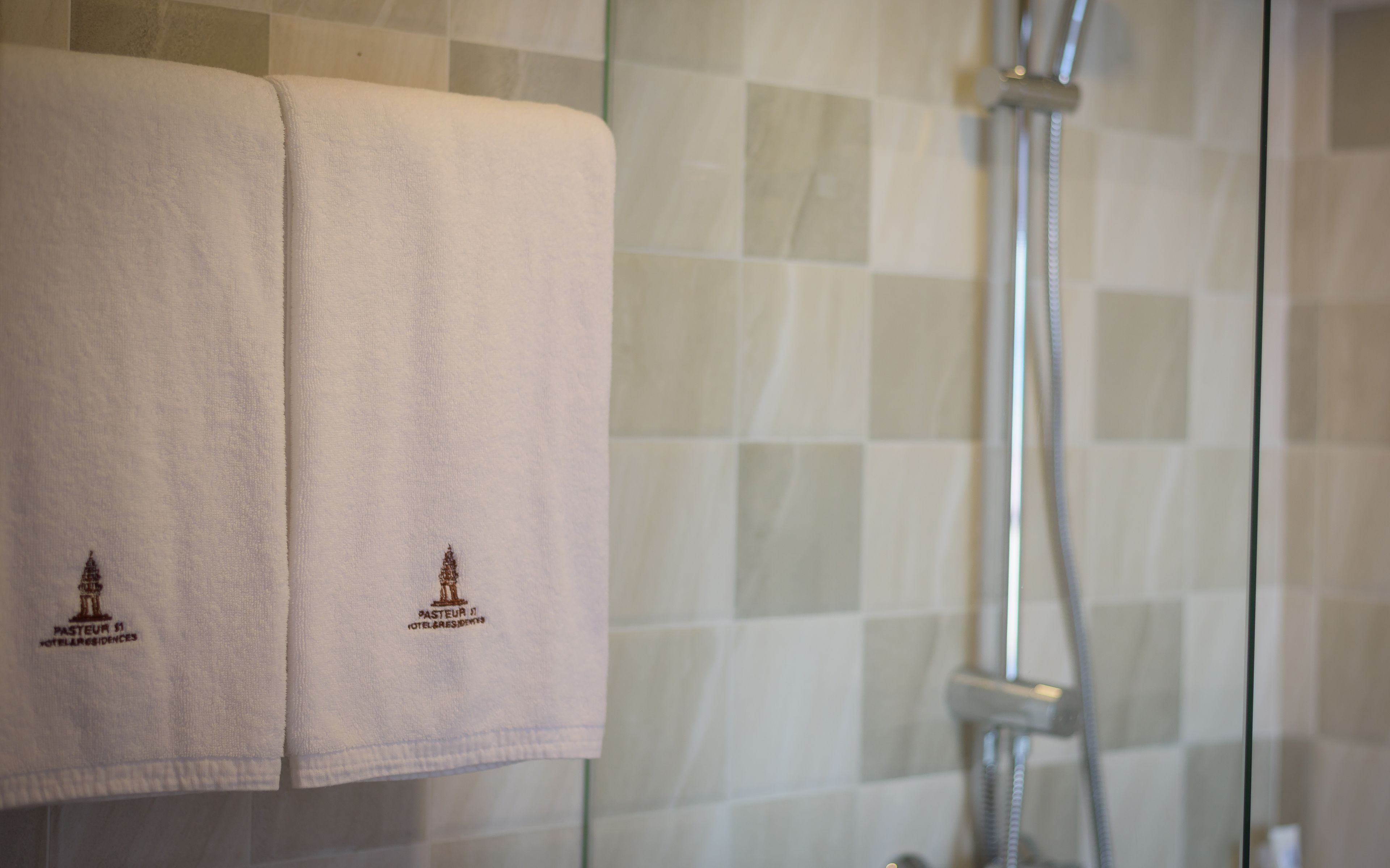 A bathroom with two towels hanging on a glass partition, a shower head, and tiled walls.